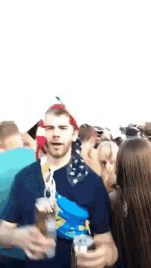 a man with a bandana on his head is standing in a crowd of people holding a can of beer .