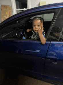 a little boy is sitting in a blue car and giving the middle finger