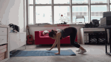 a woman stands on a yoga mat in front of a red couch with a sign on the wall that says emergency exit