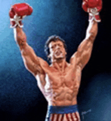 a shirtless boxer wearing red boxing gloves is raising his hands in the air .