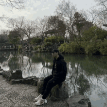 a man is sitting on a rock in front of a lake .