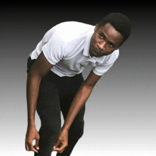 a young man wearing a white shirt and black pants is bending over