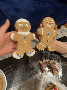 a person is holding two gingerbread men next to a bag of mars bars