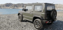 a green suzuki suv is parked on a rocky beach near the water