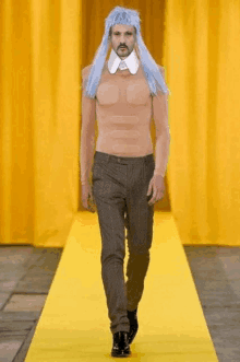 a man with a wig on his head walks down a yellow runway