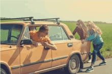 a man leaning out of a car window while two girls push the car