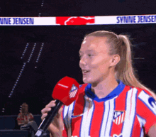 a woman in a red and white striped shirt is holding a microphone in front of a sign that says synne jensen