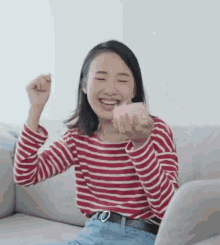 a woman in a red and white striped shirt is sitting on a couch with her fist in the air