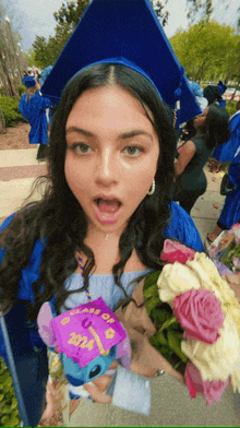 a woman in a graduation cap and gown holds a bouquet of flowers and a stuffed stitch