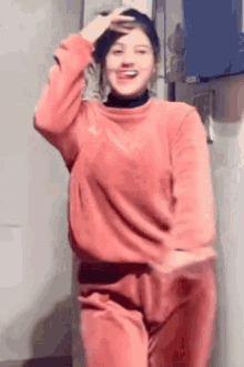 a woman in a pink sweater and pink pants is dancing in front of a refrigerator .