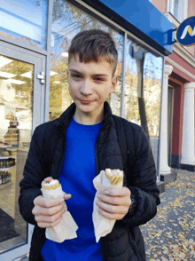 a boy is holding two sandwiches in front of a store that says subway