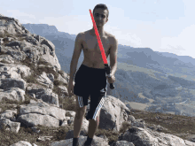 a shirtless man holding a red light saber on top of a rocky hill