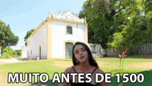 a woman stands in front of a white building with the words muito antes de 1500 on the bottom right