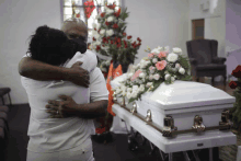 a man and woman hugging in front of a coffin