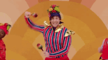 a man in a clown costume is holding a maraca and smiling while dancing .