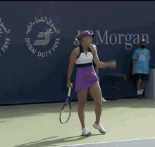 a woman in a purple skirt is holding a tennis racquet in front of a wall that says dubai duty free