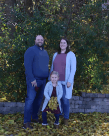 a man and woman standing next to a little girl holding leaves