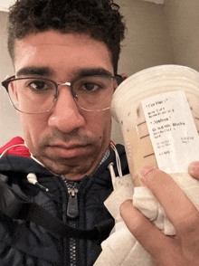 a man wearing glasses holds up a starbucks cup with a for her label on it