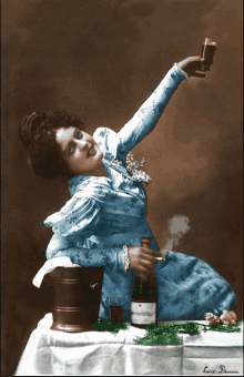 a woman in a blue dress is sitting at a table holding a bottle of prosecco