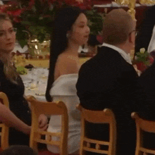 a woman in a white dress is sitting next to a man in a black suit at a dinner table .