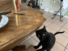 a black cat standing in front of a table with a plate of food on it