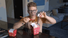 a man sitting at a table eating chinese food with chopsticks and a bottle that says ' noodles ' on it