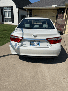 a white toyota camry is parked in front of a brick house