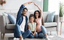 a family sits on the floor in front of a couch making a house with their hands