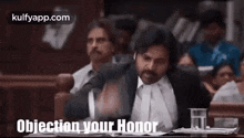 a man in a suit and tie is sitting at a table in a courtroom and giving a speech .