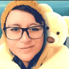 a woman wearing glasses and a yellow hat is holding a yellow teddy bear