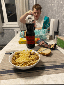 a boy sits at a table with a bowl of spaghetti and a bottle of goodbye cola