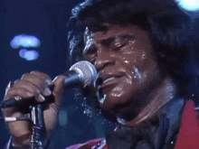 a close up of a man singing into a microphone with water on his face .