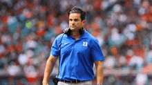 a man in a blue shirt and headphones is standing on a football field .