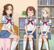 three girls in school uniforms sit on stools in front of a bookshelf with a book titled ' chinese ' on it