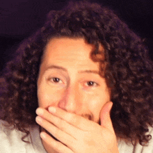 a man with curly hair and a beard covering his mouth with his hand