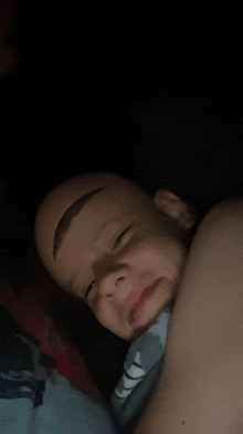 a young boy with a shaved head and eyebrows is laying in bed .