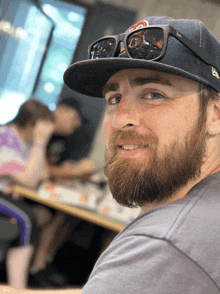 a man with a beard wearing a hat and sunglasses smiles for the camera