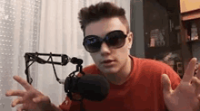 a young man wearing sunglasses is sitting in front of a microphone .