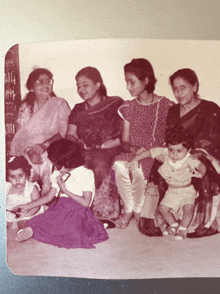 a black and white photo of a group of women and children sitting on the floor