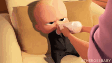 a baby in a suit is drinking milk from a bottle while laying on a couch .