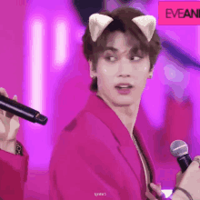 a man in a pink jacket is holding a microphone and wearing cat ears on his head .