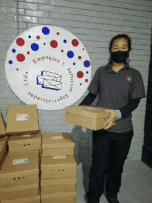 a woman wearing a mask holds a box in front of a sign that says empaques y servicios especializados