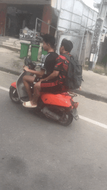 two young men are riding a red scooter on a street