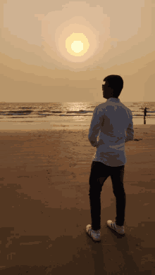 a man standing on a beach looking at the sun setting