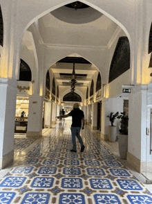 a man in a black shirt walks down a hallway with a blue and white tile floor