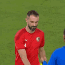 a man with a beard is wearing a red t-shirt and holding a yellow flag on a soccer field .