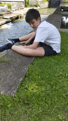 a young boy is stretching his legs in the grass near a waterfall