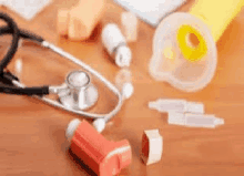 a stethoscope , inhaler , pills , and other medical supplies are on a wooden table .