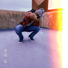 a man wearing a plaid shirt and a gray beanie is squatting down with the date of february 21 on the bottom right