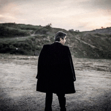 a man in a black coat is standing in the middle of a field